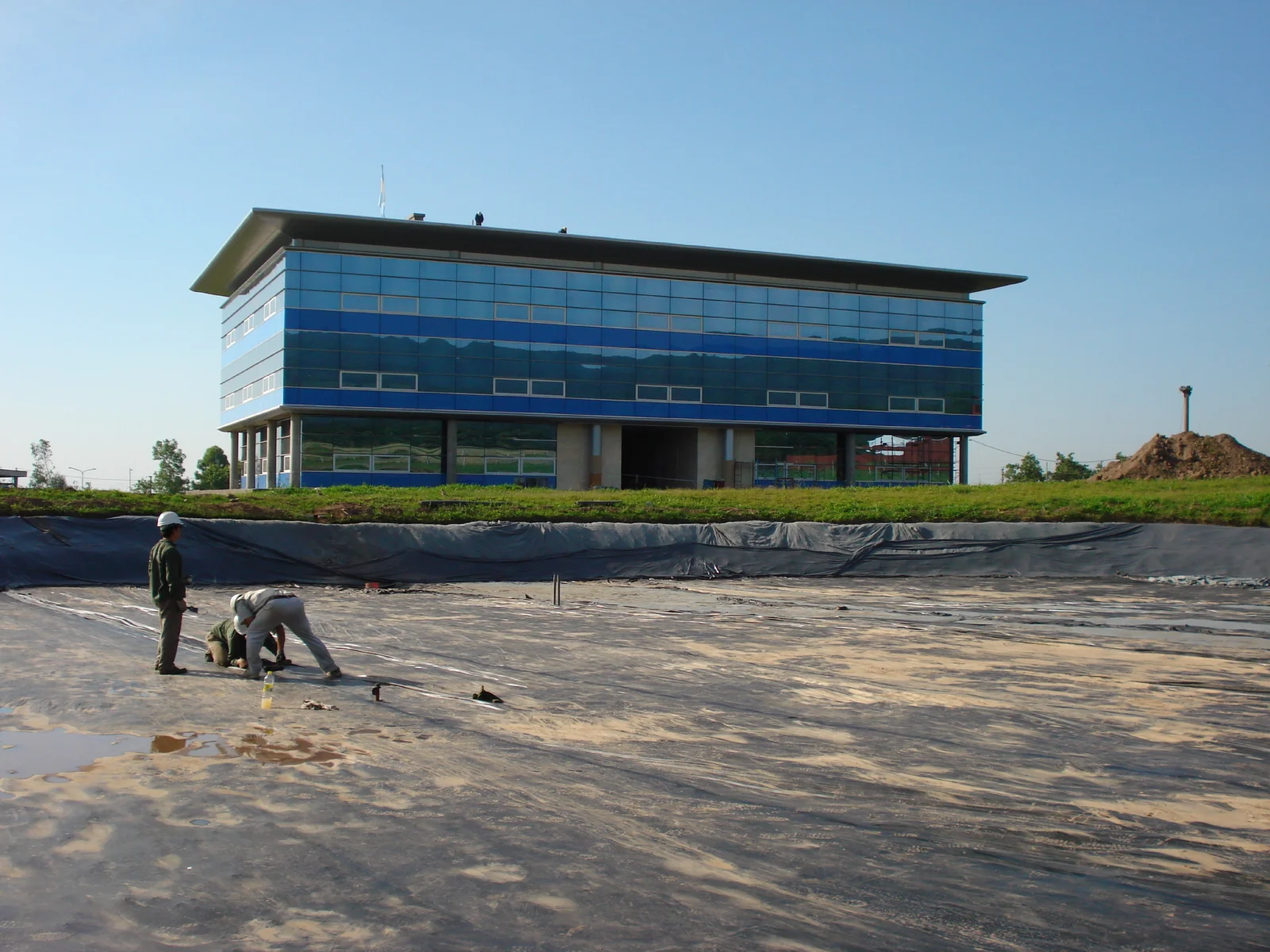 Preparación del terreno para impermeabilizar una laguna junto a un edificio corporativo